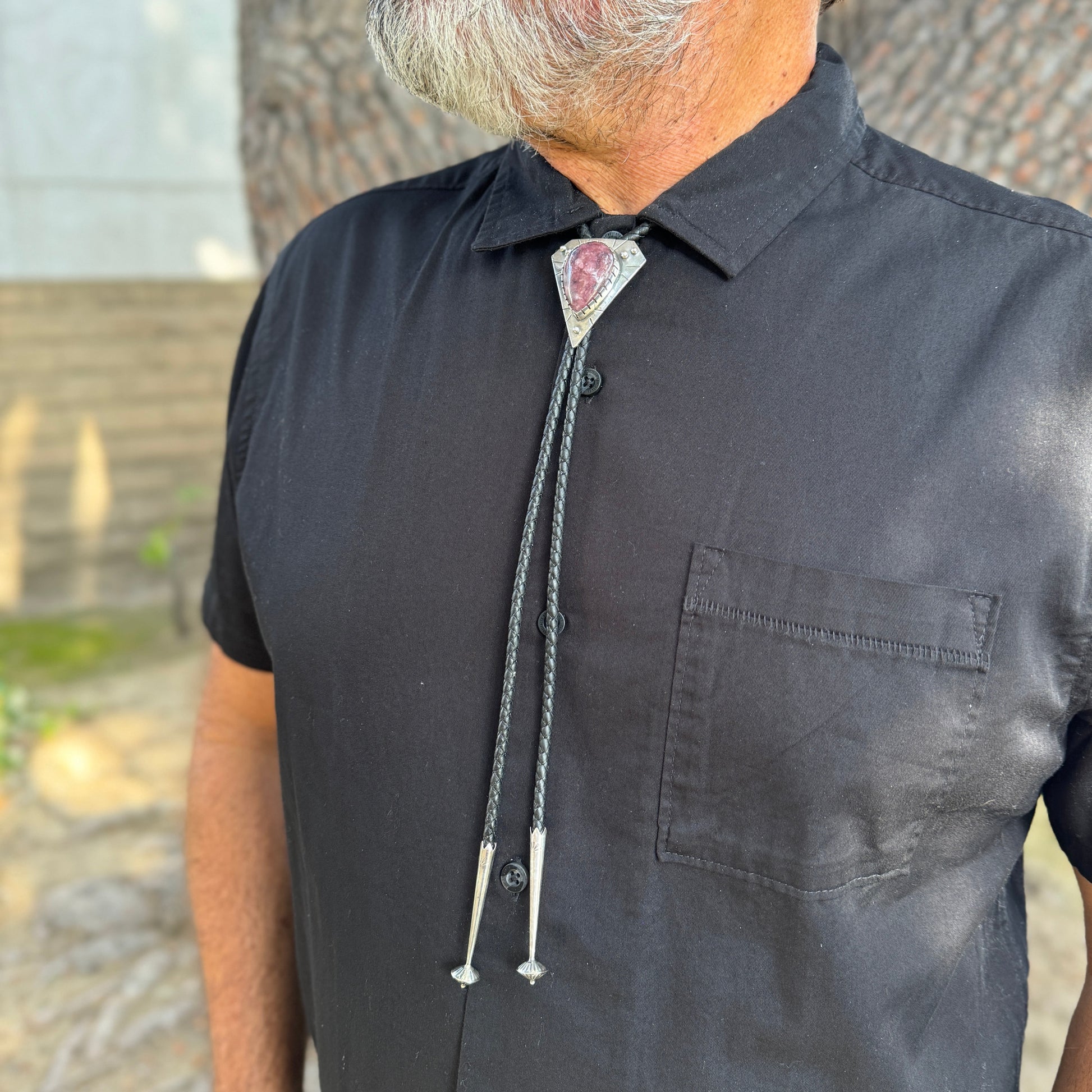photo of a mans chest wearing black collared shirt and a triangle silver lepidolite bolo tie