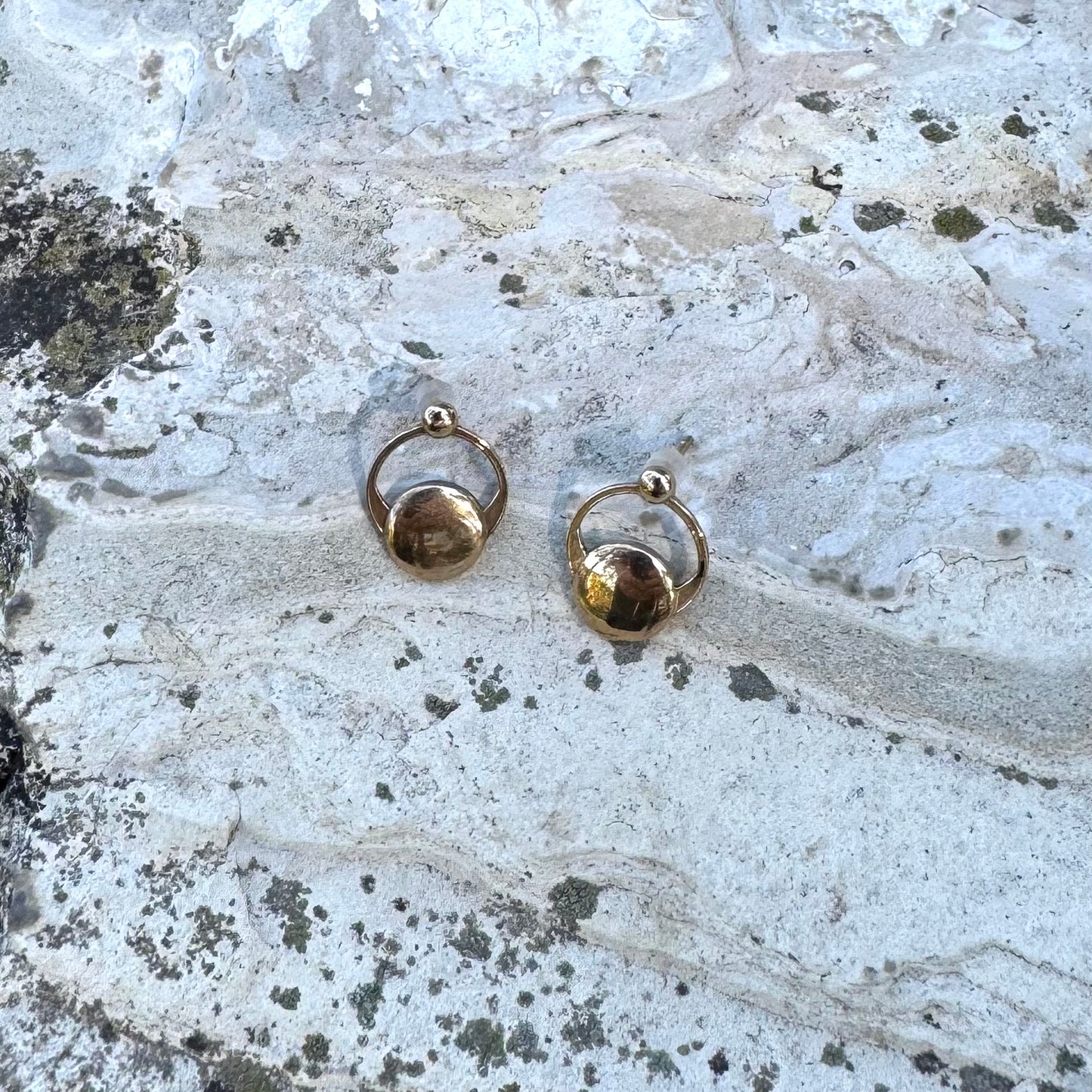 Gold-toned crop circles earrings on a textured stone surface