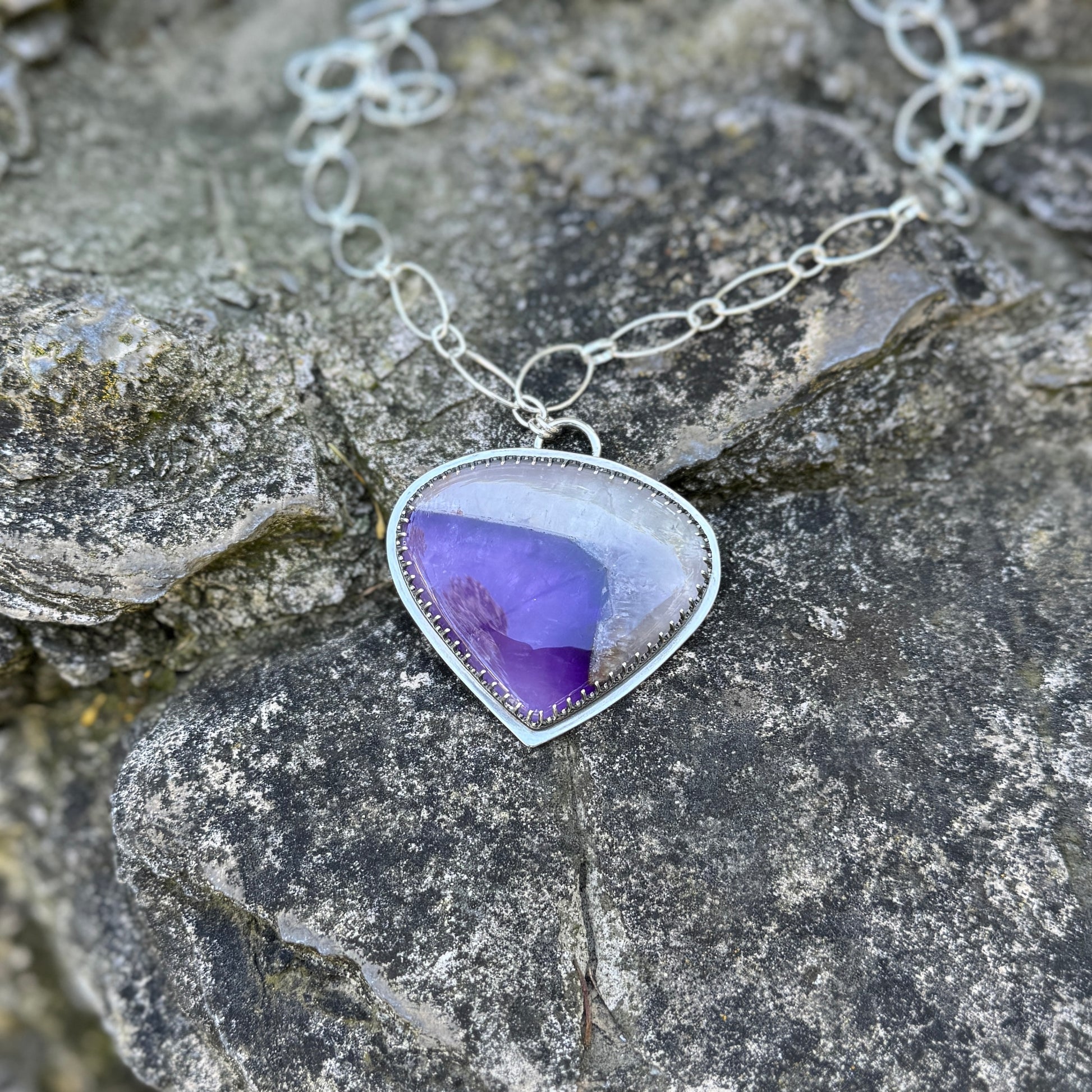 picture of a silver amethyst necklace on a dark rock 