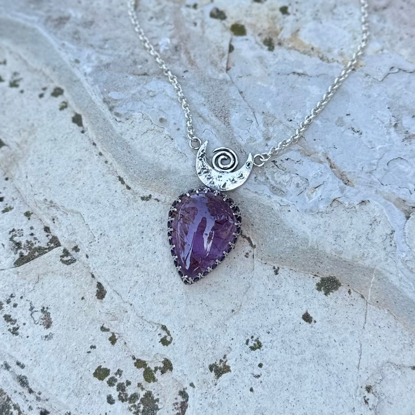 Necklace with a purple pendant and silver chain on a textured stone surface