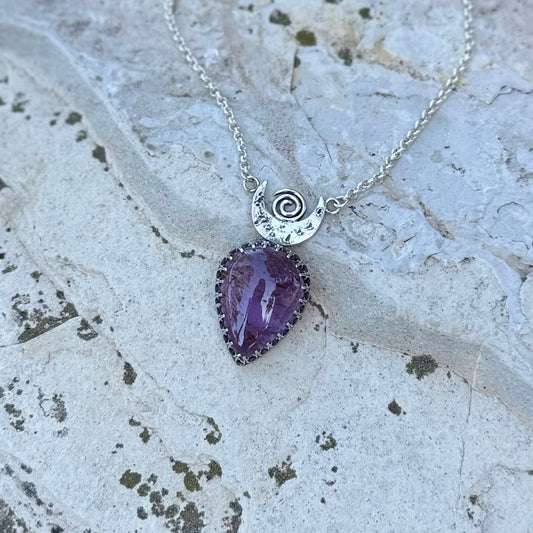 Necklace with a purple pendant and silver chain on a textured stone surface