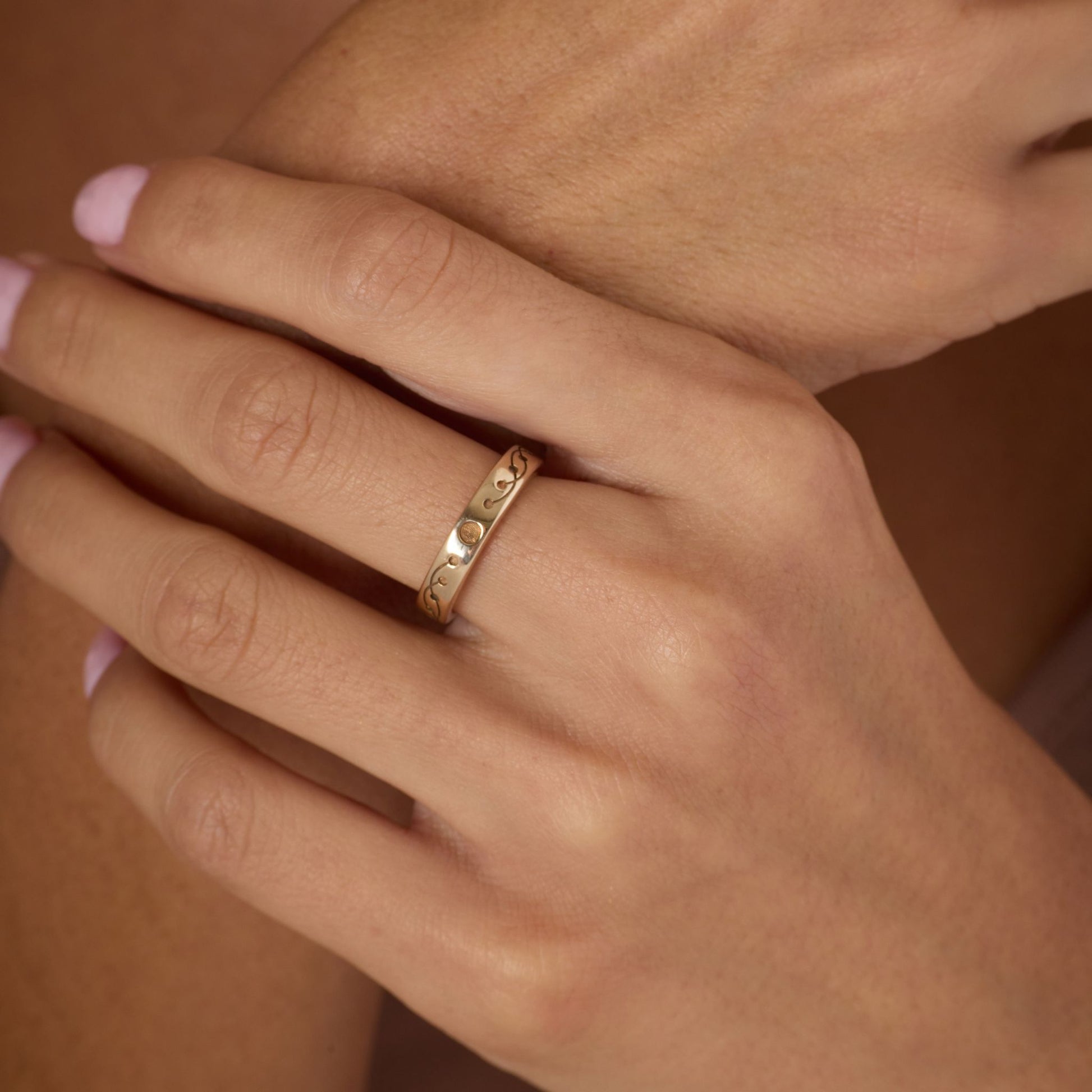Gold-toned ring on a person's finger with a warm brown background