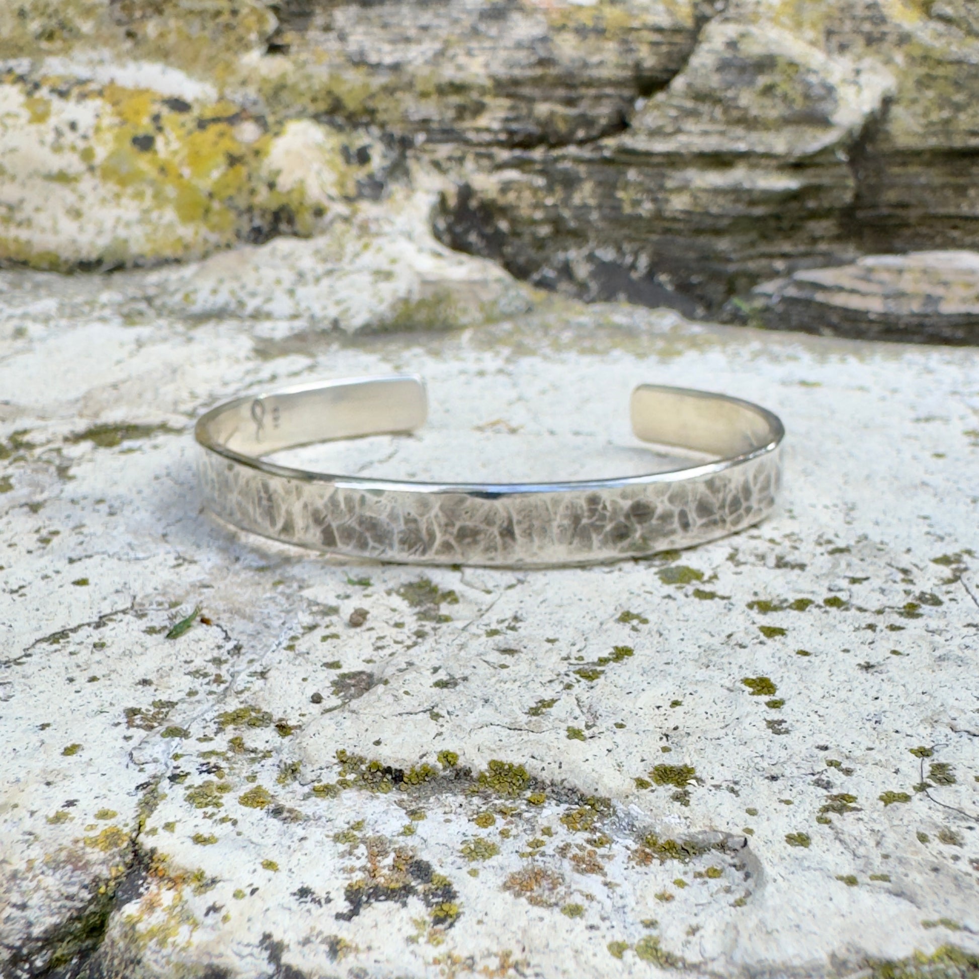 photo of a thick silver cuff bracelet with a hammered texture on a white rock