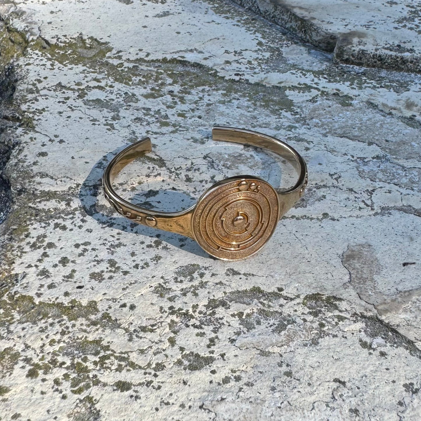 Gold-toned bracelet with a circular design on a textured stone surface