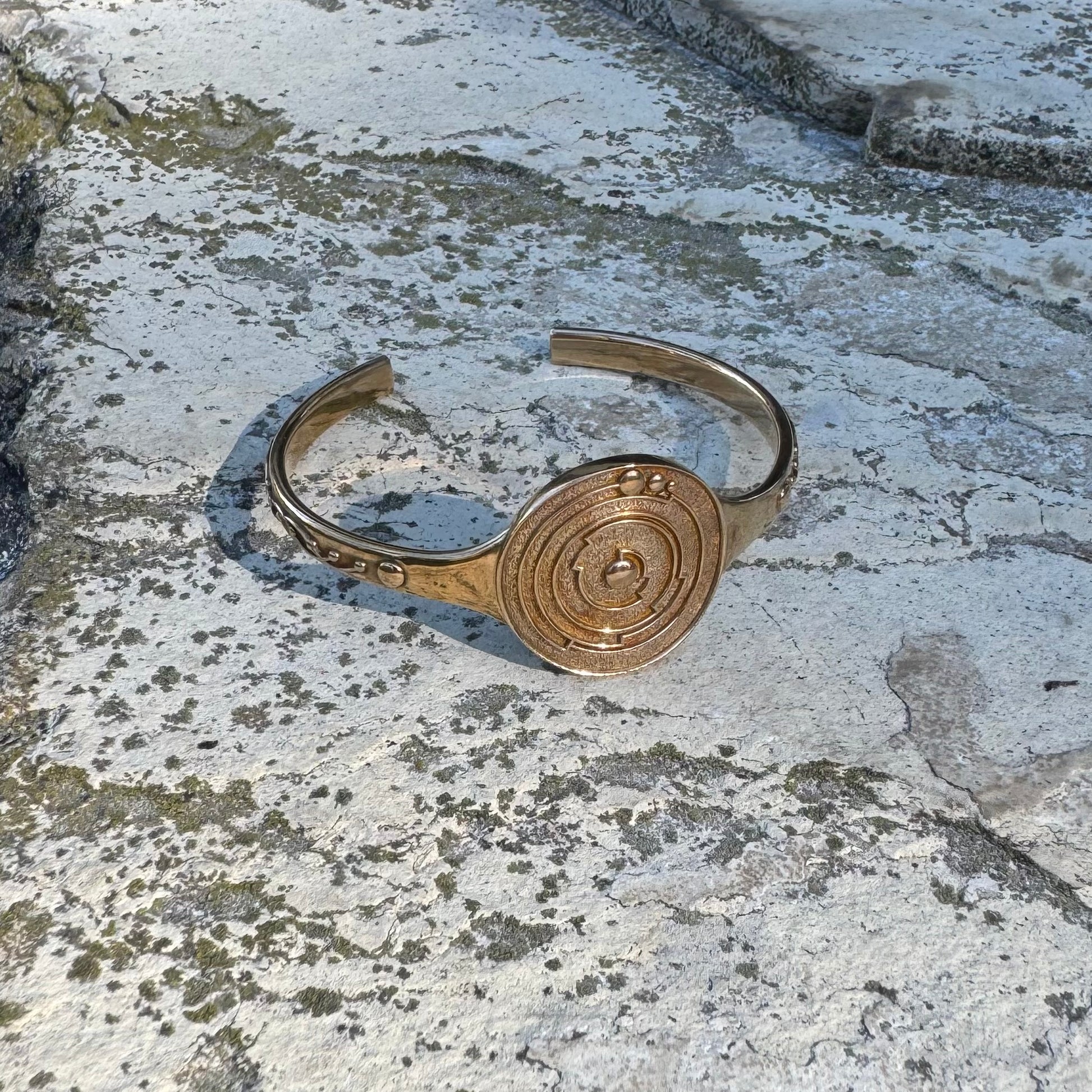 Gold-toned bracelet with a circular design on a textured stone surface