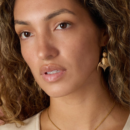 Close-up of a woman wearing gold-toned earrings and a necklace with a neutral background