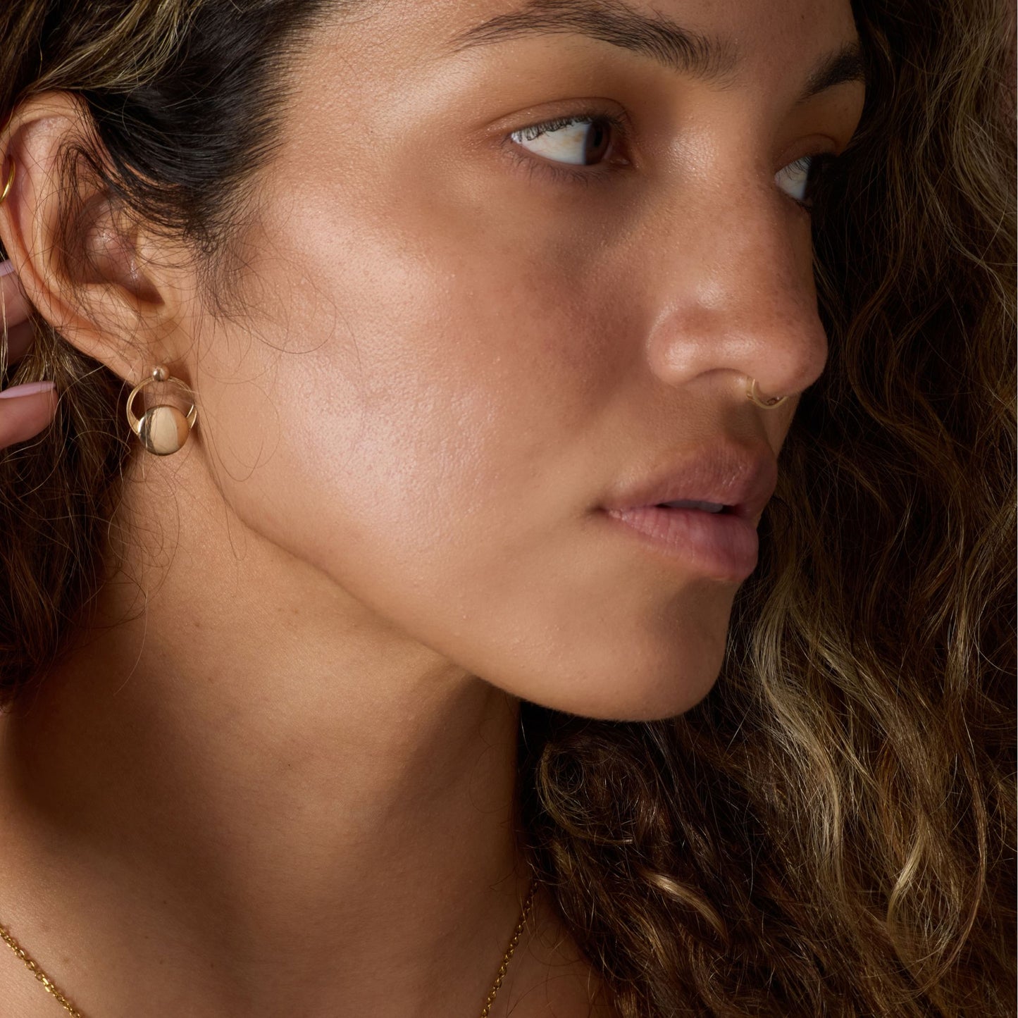 Close-up of a woman wearing gold earrings and a nose ring with a blurred background