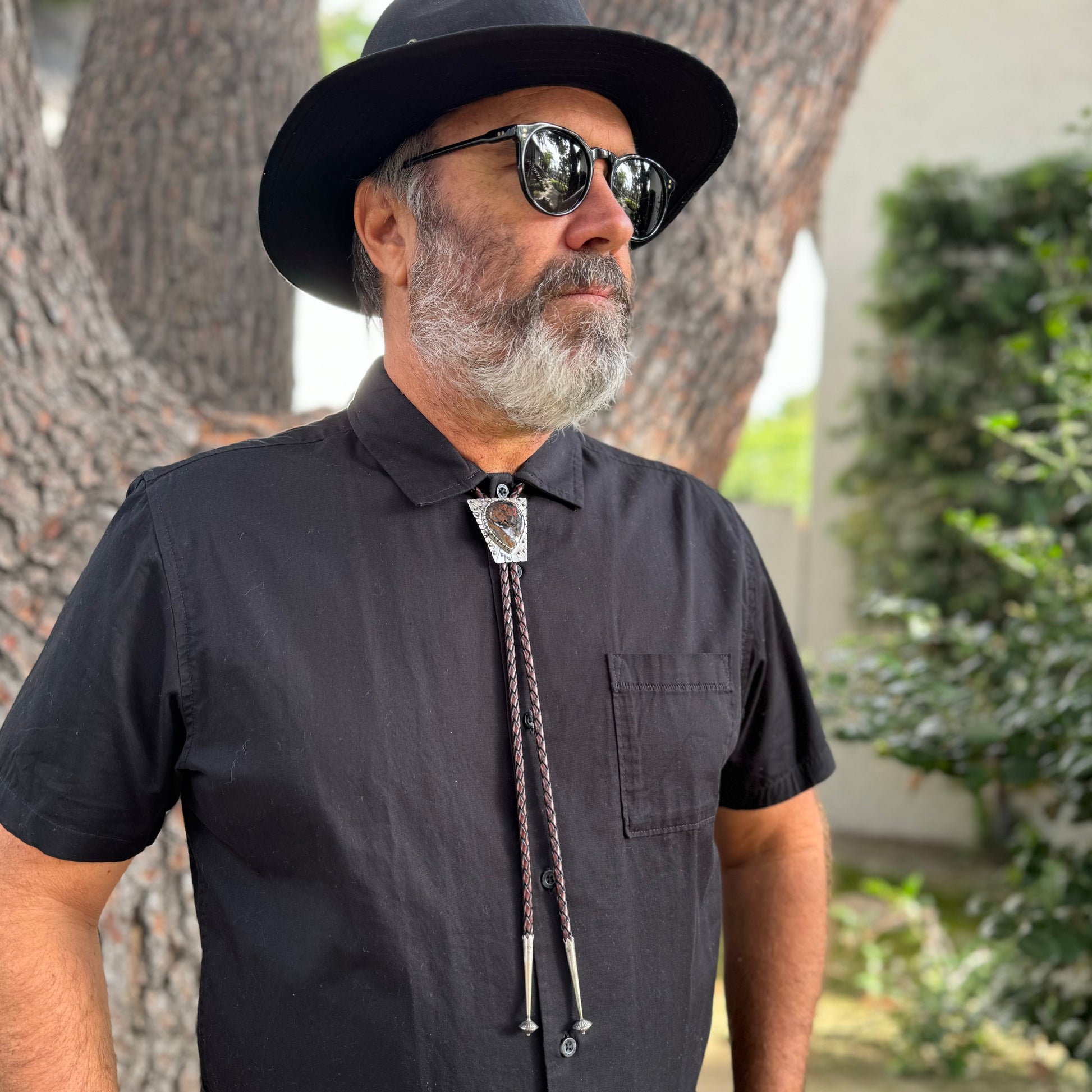 photo of a mans chest wearing black collared shirt and a triangle silver peitersite bolo tie 