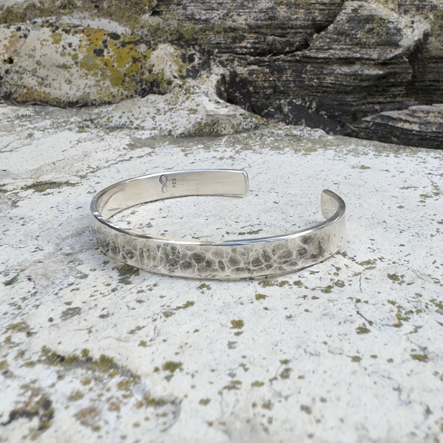 photo of a thick silver cuff bracelet with a hammered texture on a white rock