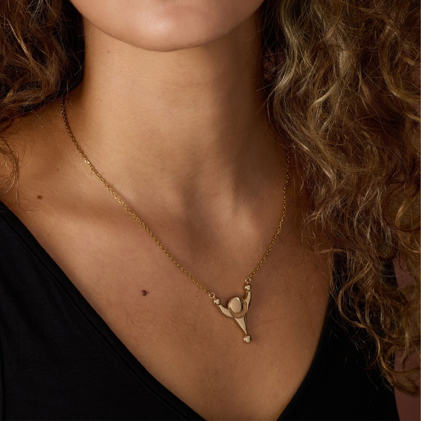 Close-up of a person wearing a gold-toned necklace with a crop circle pendant.