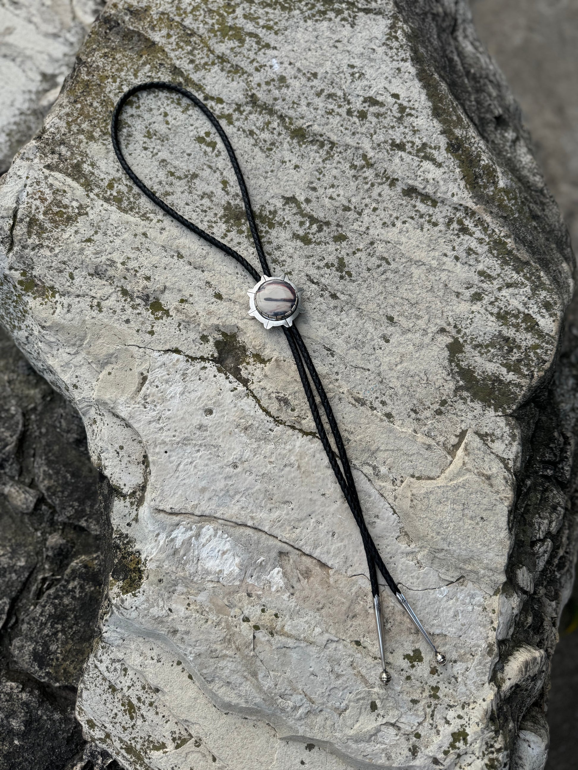 photo of a silver round white and gray sci-fi jasper bolo tie on a white rock