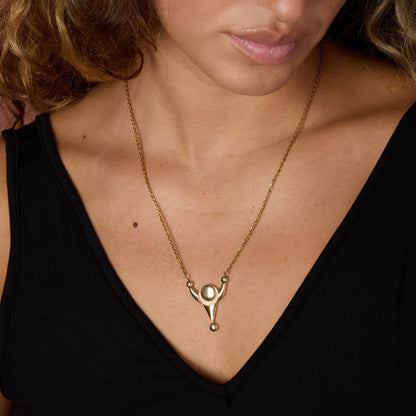 Close-up of a woman wearing a gold-toned necklace with a unique pendant.
