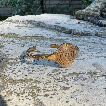 Gold-toned cuff bracelet with a crop circle design on a stone surface
