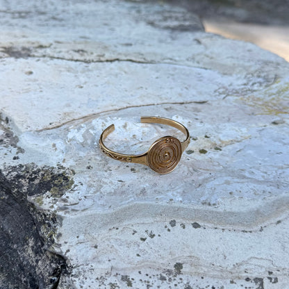 Gold-toned cuff bracelet with circular design on a textured stone surface