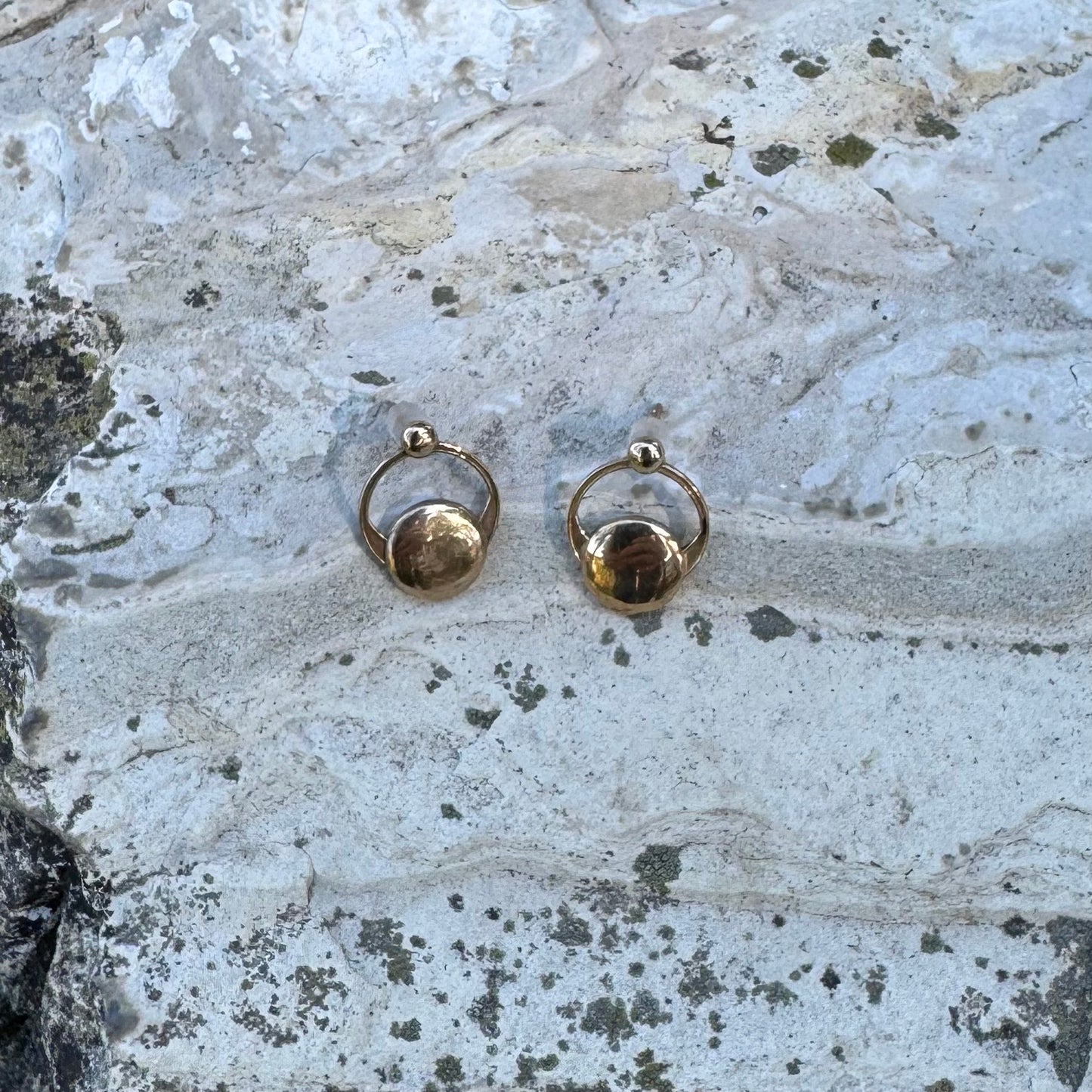 Gold hoop earrings on a textured stone surface
