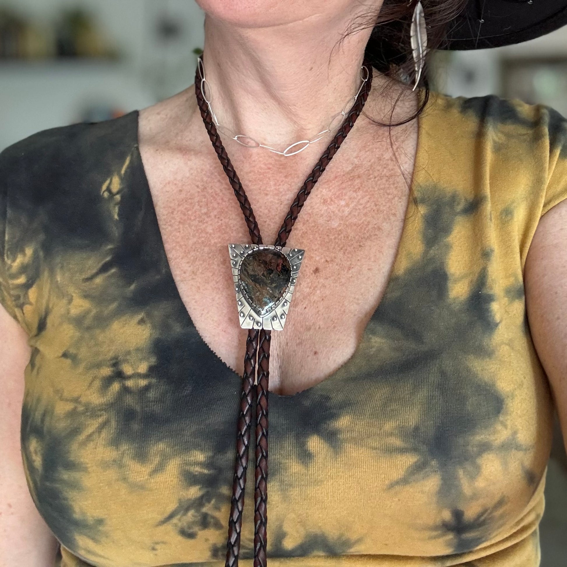 photo of a woman wearing yellow and black tye-dyed shirt and a large silver peitersite bolo tie with spheres