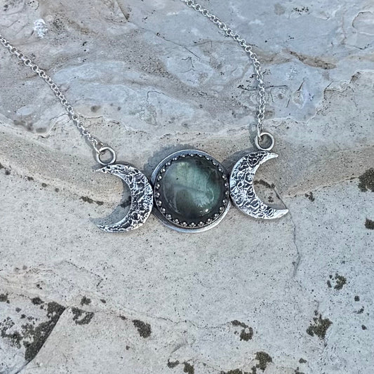 Necklace with a central stone and crescent moon pendants on a stone surface