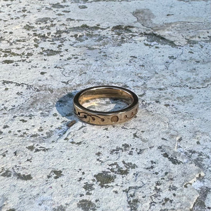 Gold ring with engraved wavy, crop circle design on a textured stone surface 