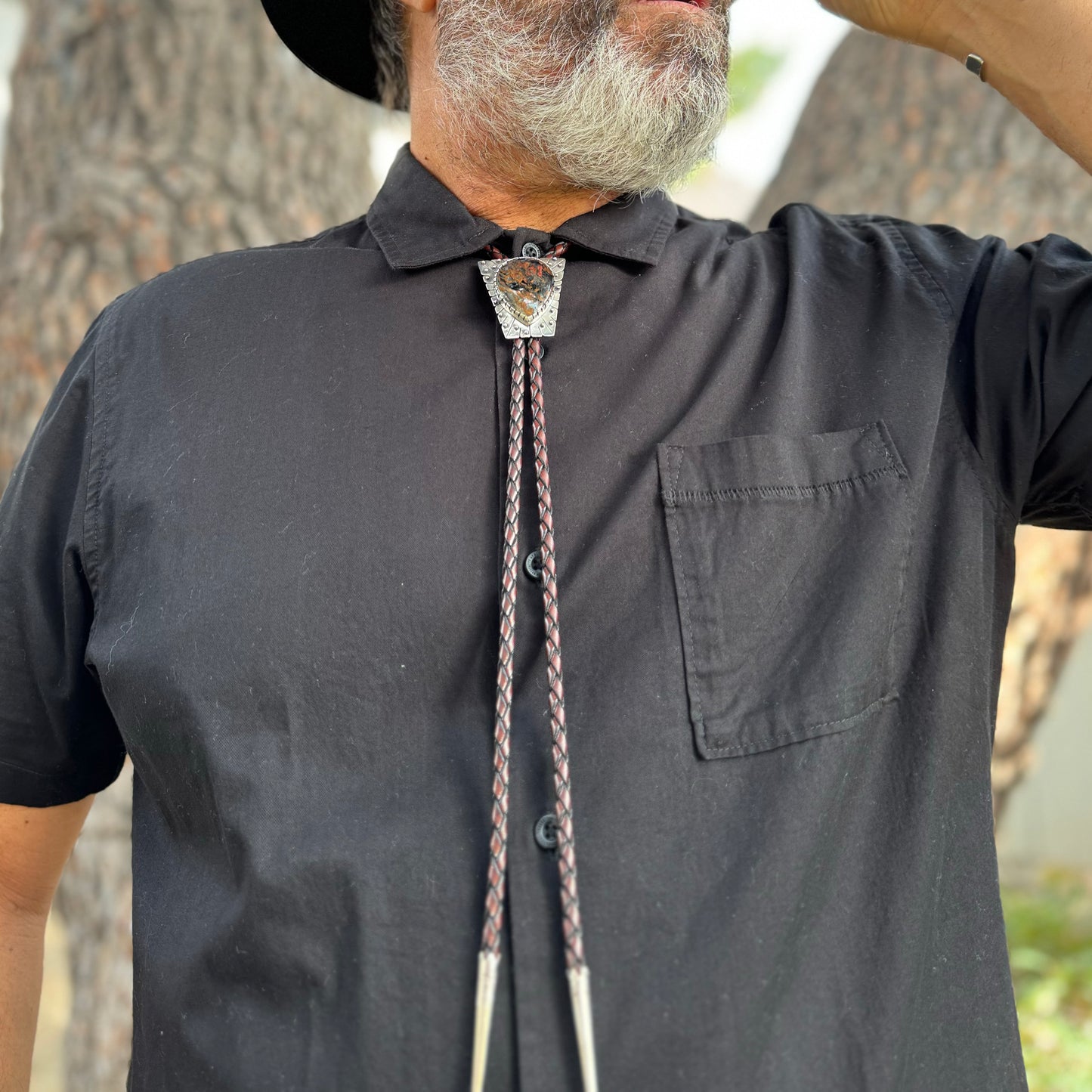 photo of a man's chest wearing black collared shirt and a triangle silver peitersite bolo tie 