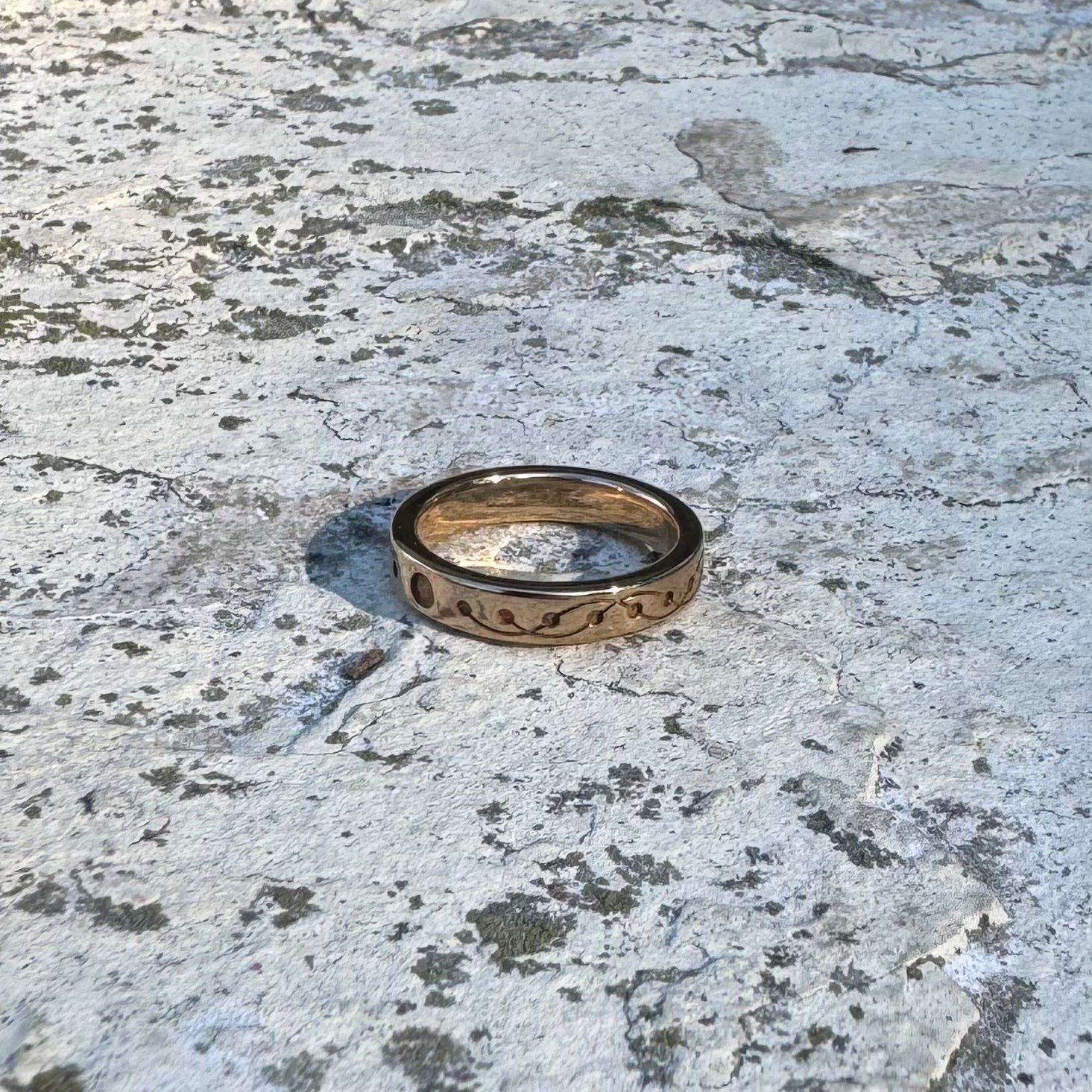 Gold-toned  ring with engraved design on a textured stone surface