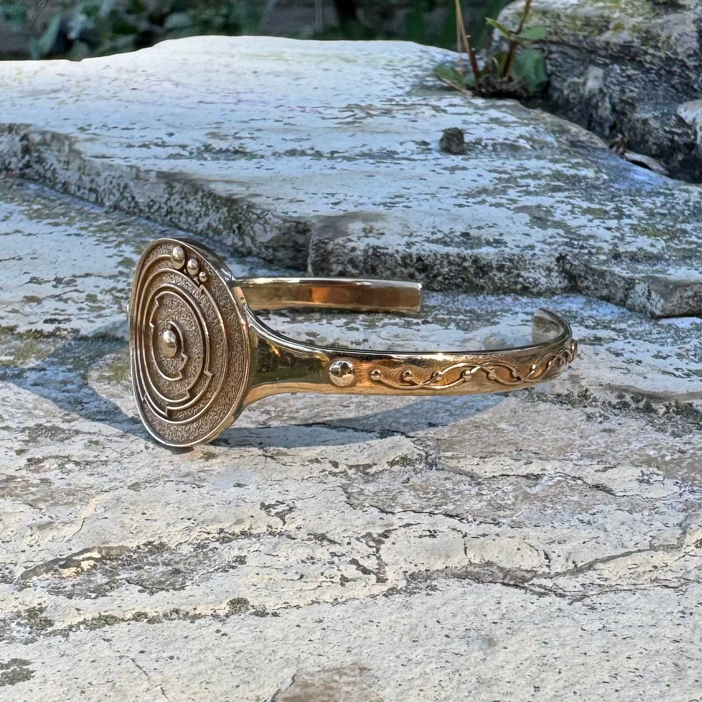 Gold-toned bracelet with crop circle design on a stone surface