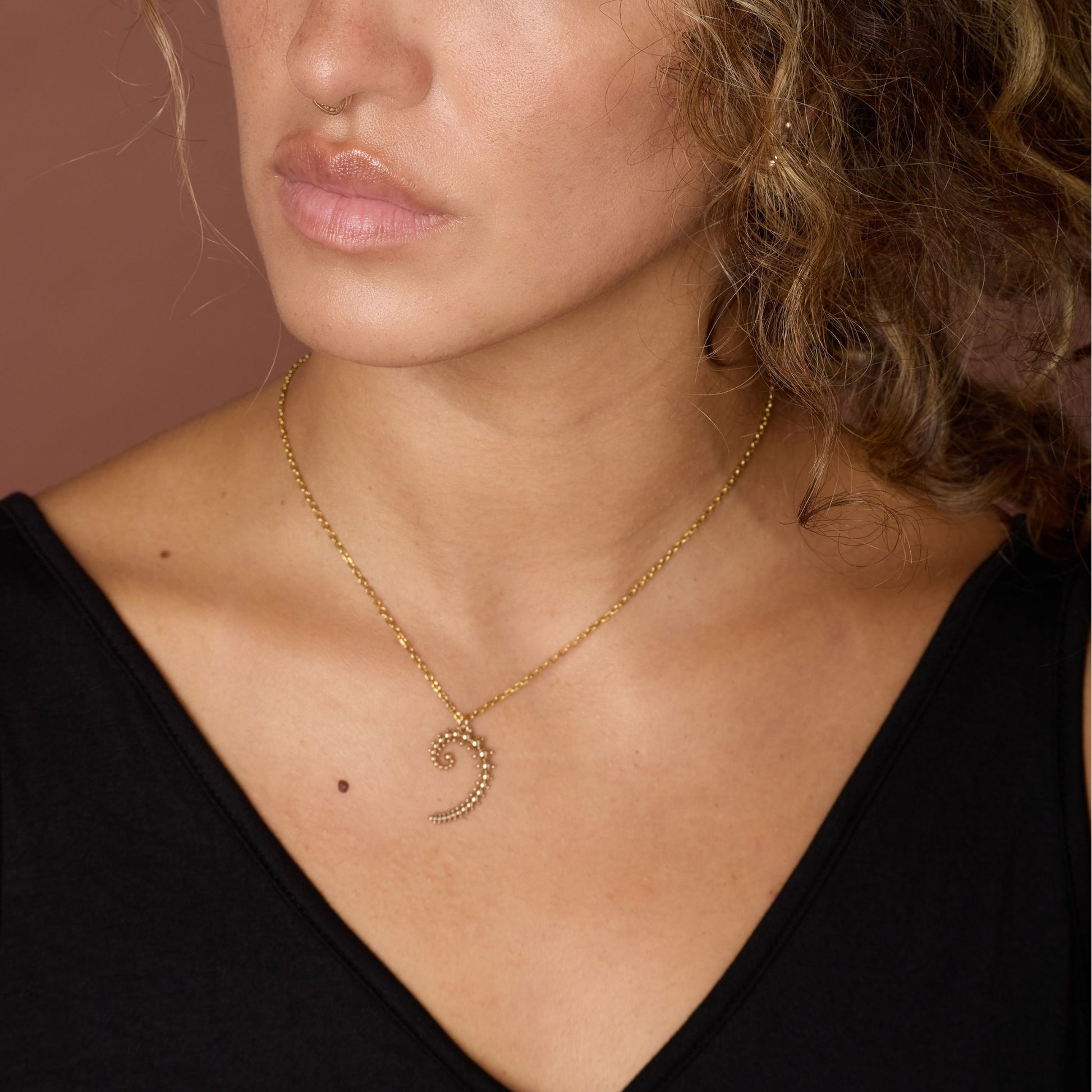 Close-up of a person wearing a gold-toned necklace with afibonacci pendant against a brown background.
