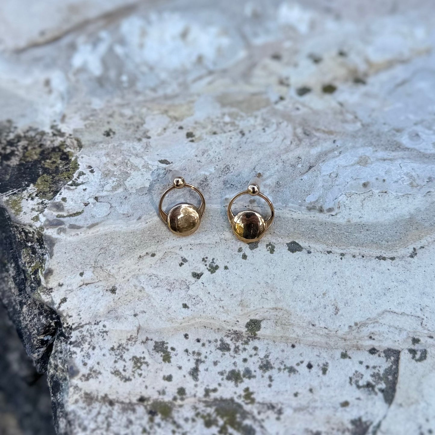 Gold-toned crop circleb earrings on a textured stone surface