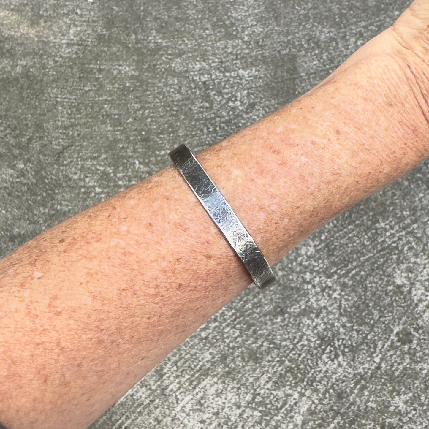 photo of a womans forearm wearing a silver cuff bracelet with a rustic hammered texture