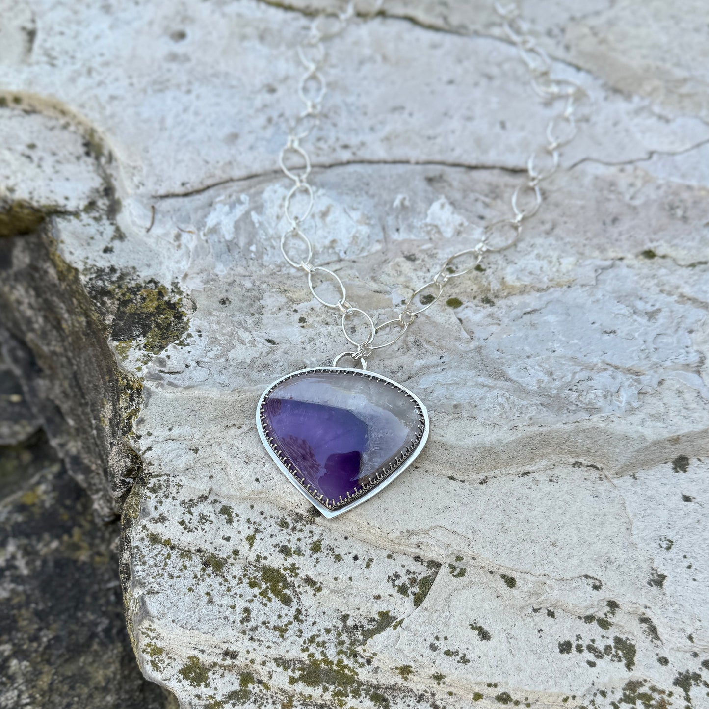 picture of a silver amethyst quartz necklace on a rock 