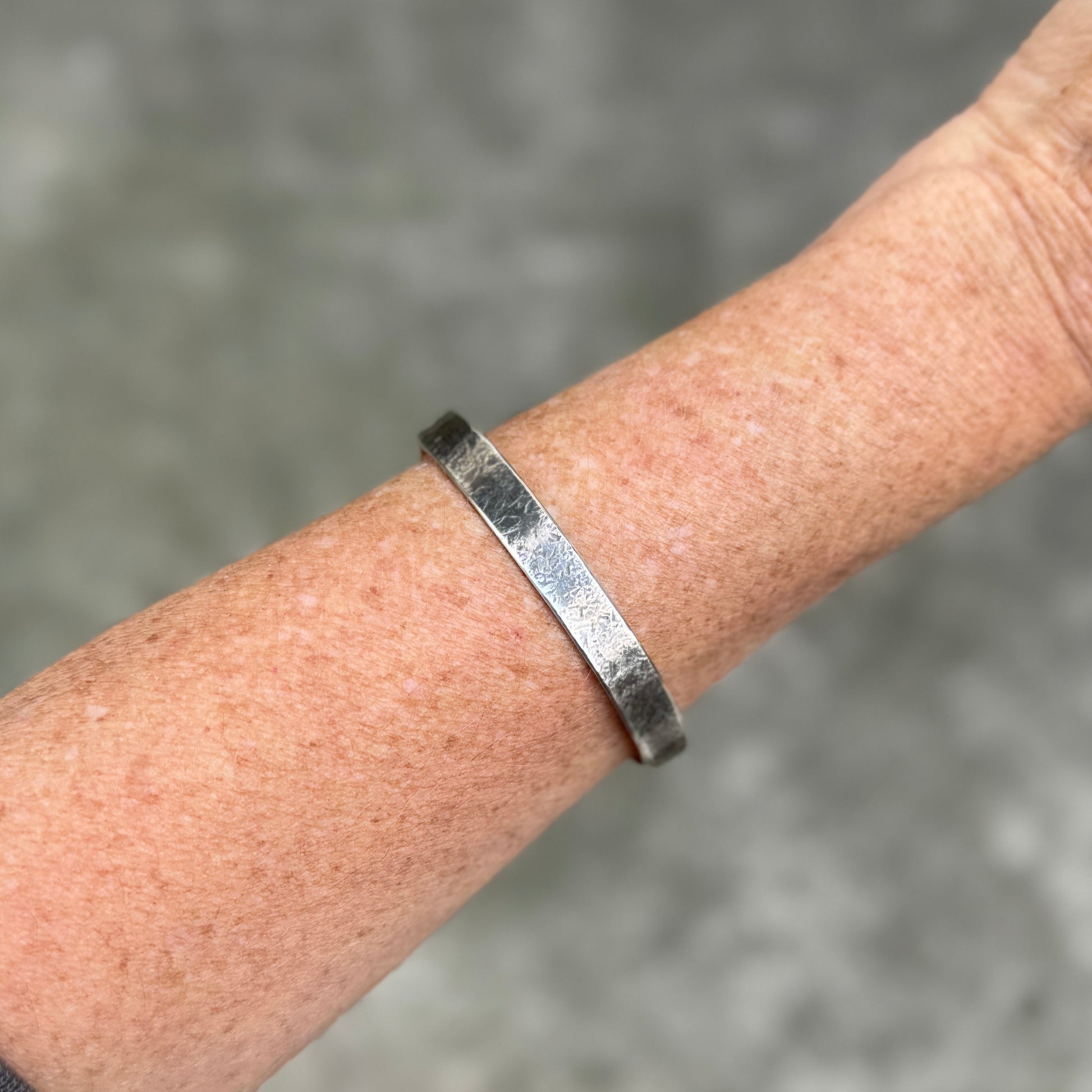 photo of a womans forearm wearing a silver cuff bracelet with a rustic hammered texture