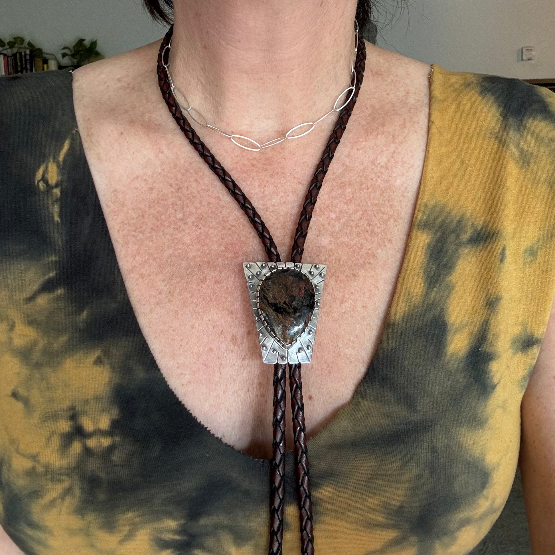 photo of a woman wearing yellow and black tye-dyed shirt and a large silver peitersite bolo tie with spheres