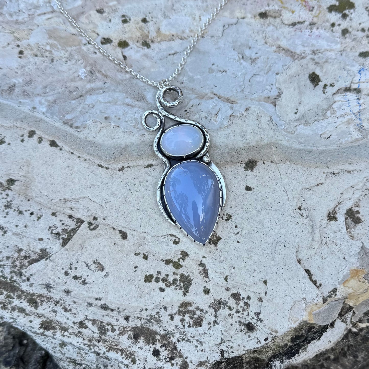 Silver necklace with a blue pendant on a textured stone surface