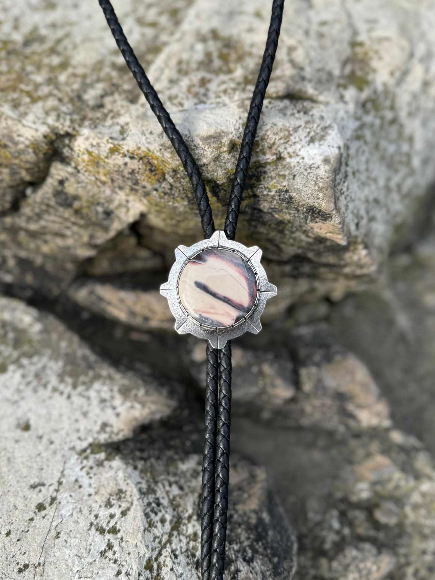 photo of a silver round white and gray sci-fi jasper bolo tie on a dark rock