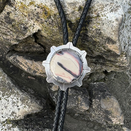 photo of a silver round white and gray sci-fi jasper bolo tie on a dark rock