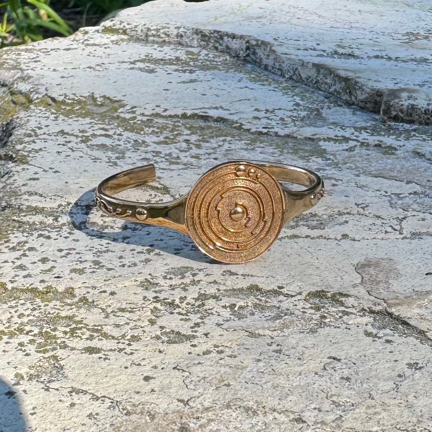 Gold cuff bracelet with crop circle design on a stone surface