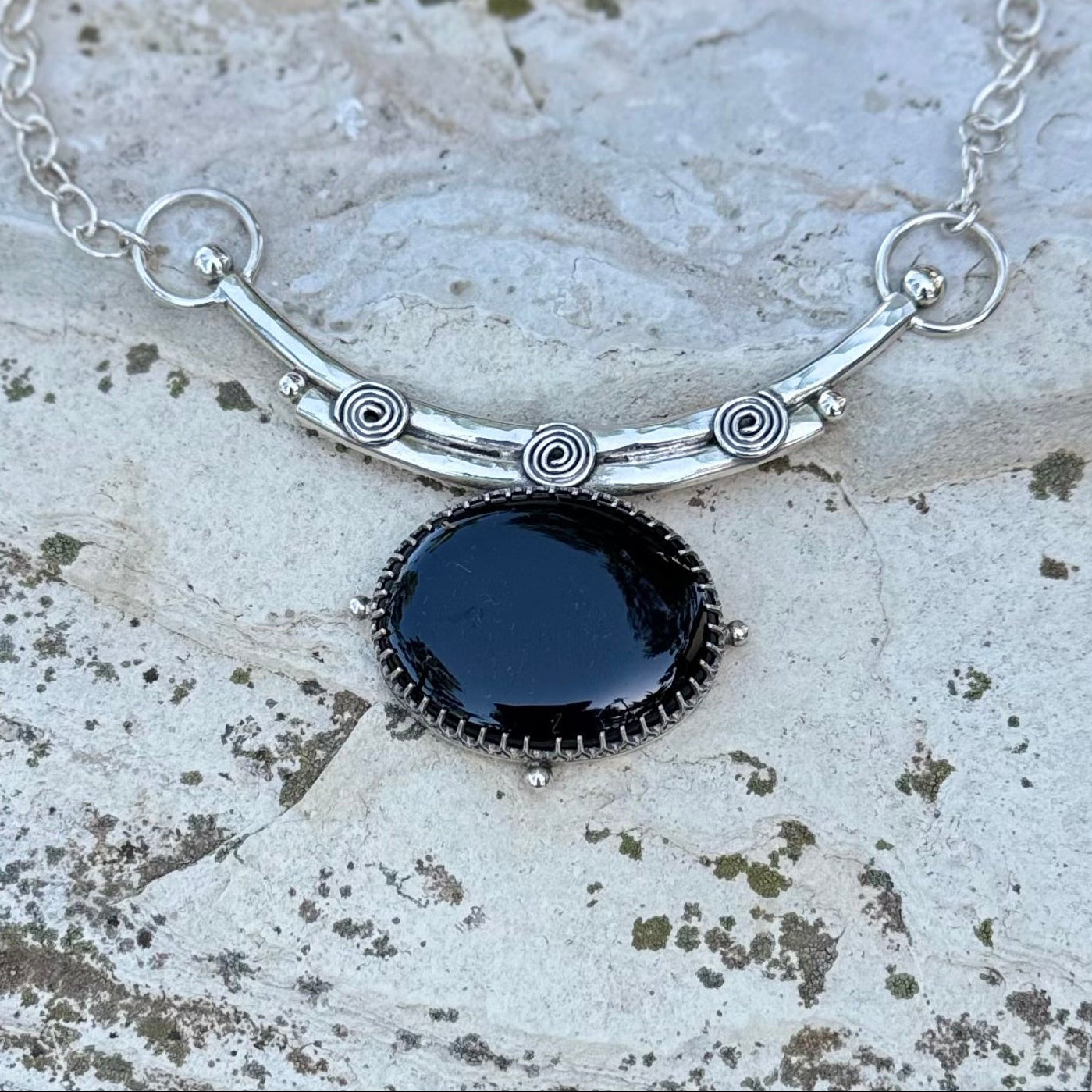 Silver necklace with a black pendant on a textured stone surface