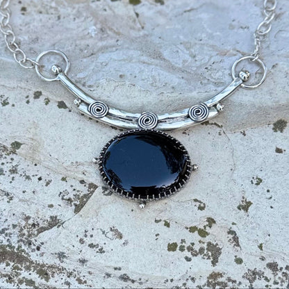 Silver necklace with a black pendant on a textured stone surface