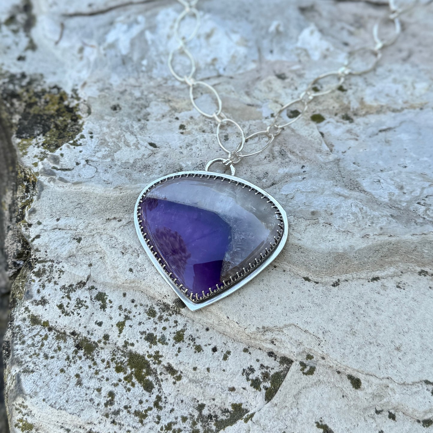 picture of a silver amethyst quartz necklace on a rock 