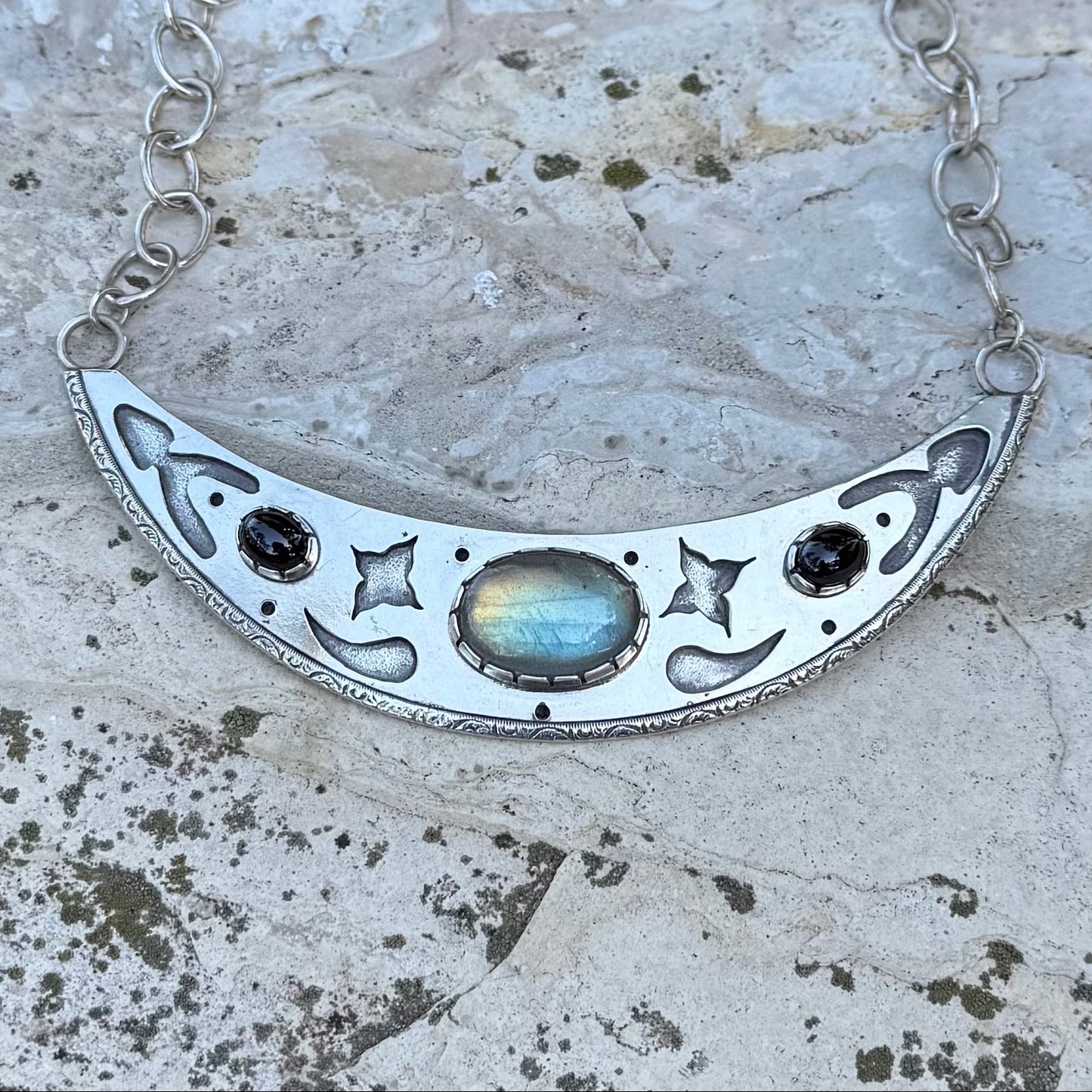 Silver necklace with a crescent moon design on a textured stone surface