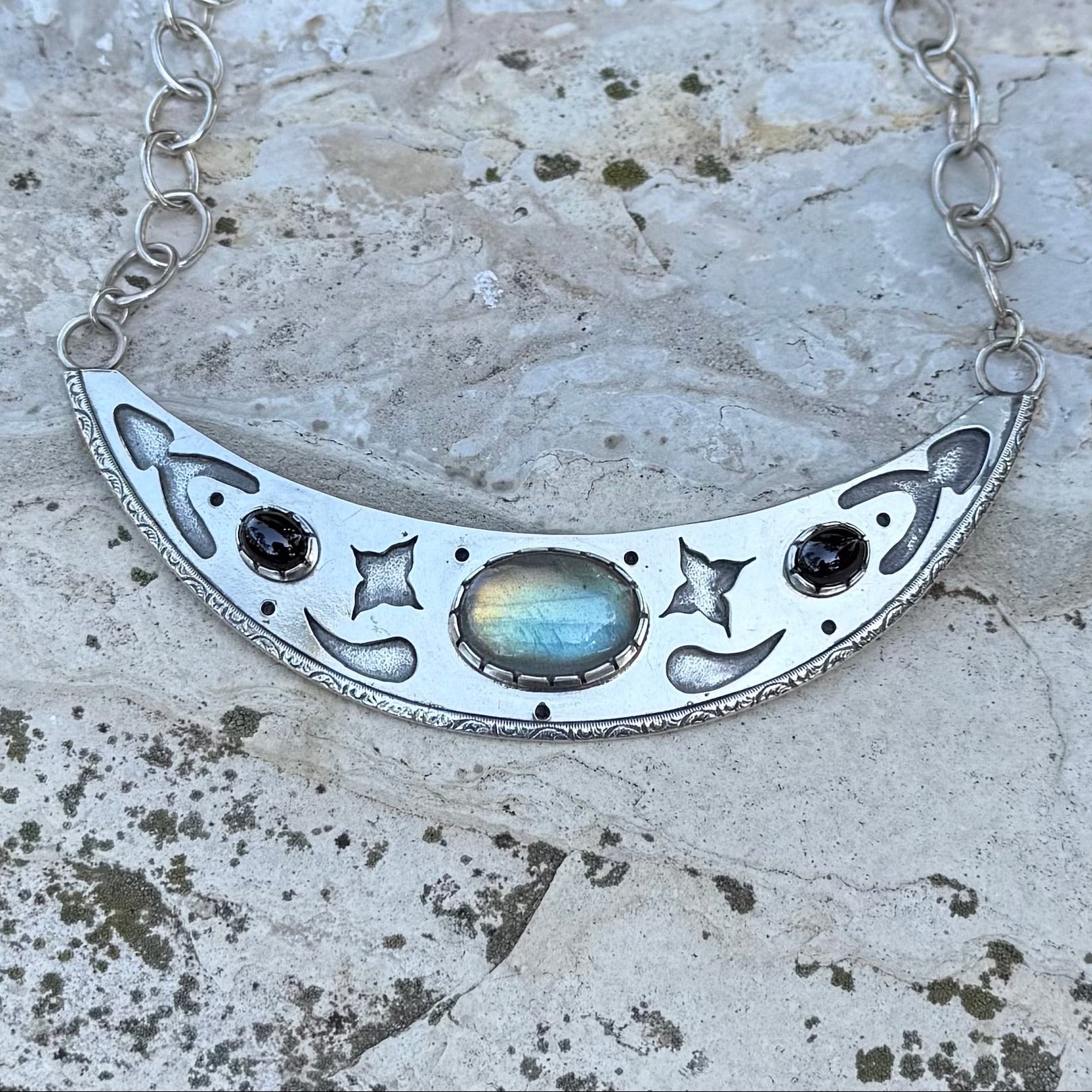 Silver necklace with a crescent moon design on a textured stone surface