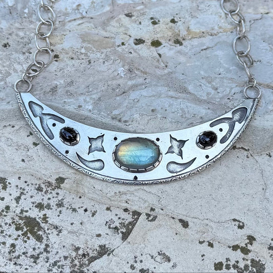 Silver necklace with a crescent moon design on a textured stone surface