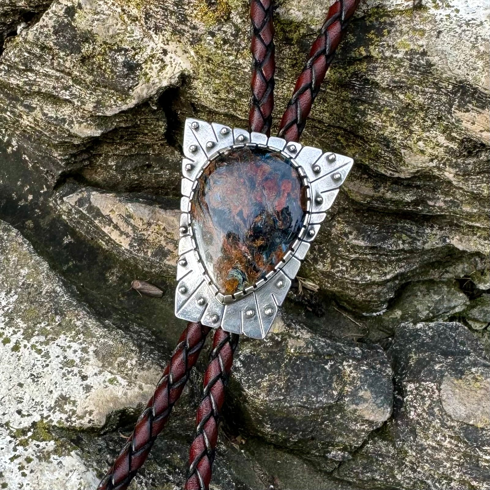 photo of a unique silver pietersite bolo tie on a dark rock