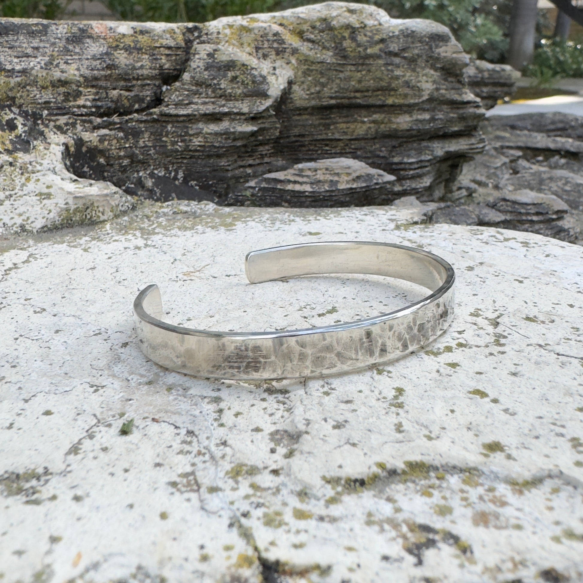 photo of a thick silver cuff bracelet with a hammered texture on a white rock