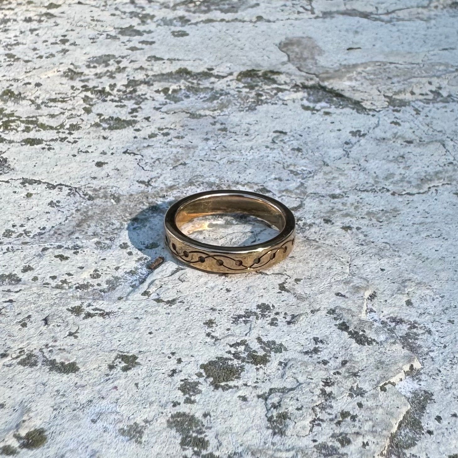 Gold-toned  ring with intricate crop circle design on a textured stone surface