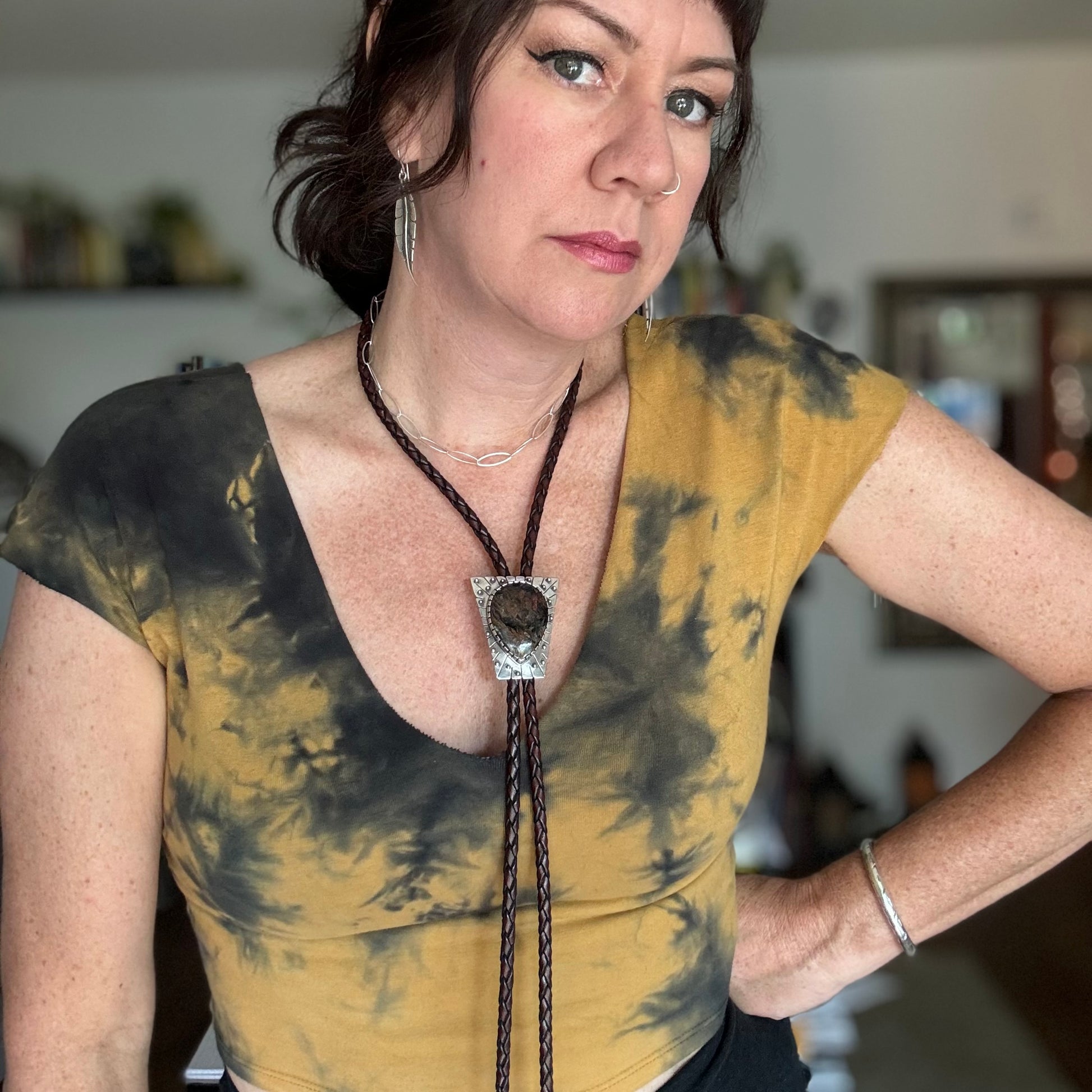 photo of a woman wearing yellow and black tye-dyed shirt and a large silver peitersite bolo tie with spheres