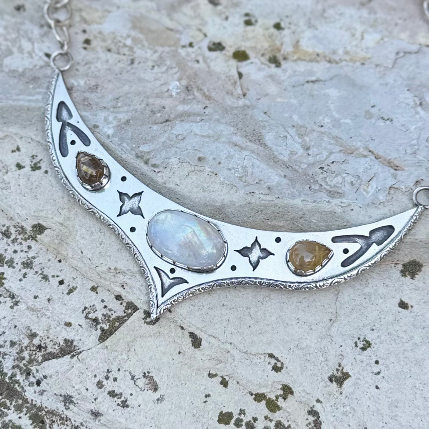 Silver necklace with moonstone and other stones on a textured stone surface