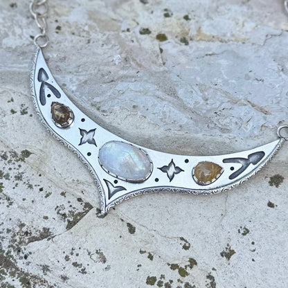 Silver necklace with moonstone and other stones on a textured stone surface