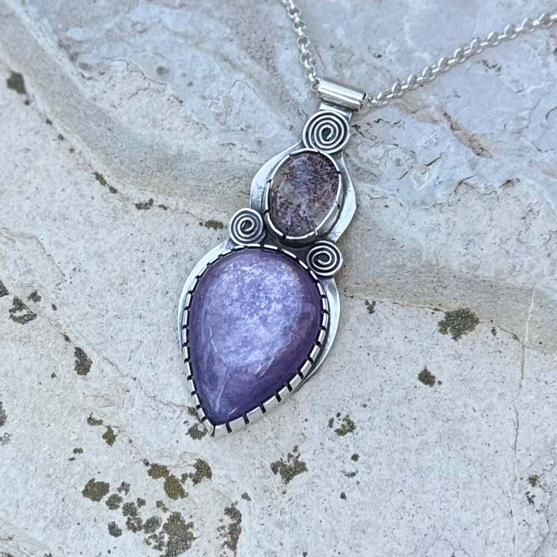 Purple teardrop pendant with silver detailing on a stone surface