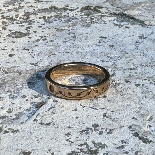 A gold-toned band ring with a wavy, crop circle design, resting on a textured, weathered stone surface.