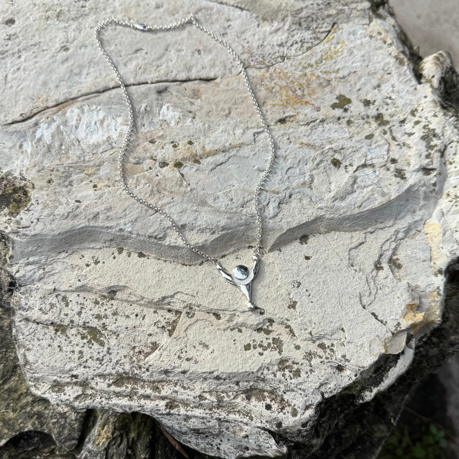 A silver necklace with a small pendant featuring a circular inset, displayed on a textured light gray stone surface.